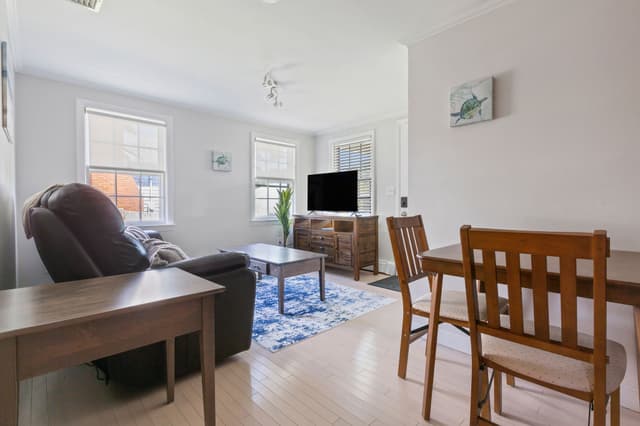 Living room with a dark leather recliner, coffee table, blue and white rug and TV on a wood console; a dining table at right.