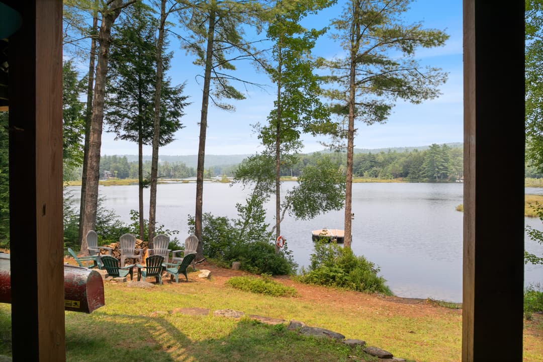 Lawn sloping to a lake with a fire pit ringed by Adirondack chairs, stacked firewood and a floating swim platform.