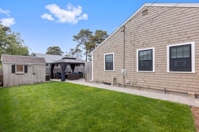 Grassy fenced backyard beside the shingled house, with a storage shed and a curtained gazebo lounge in the back corner.
