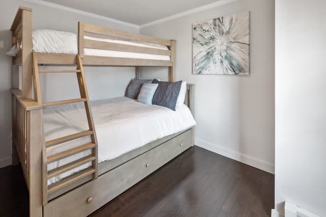 Bedroom with a wooden twin-over-full bunk bed with ladder, under-bed drawers, white bedding and gray pillows.